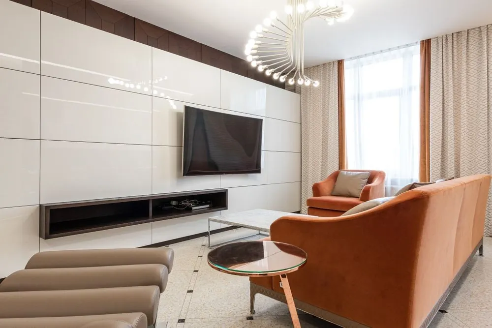 Sala de estar com sofá laranja e painel de TV claro